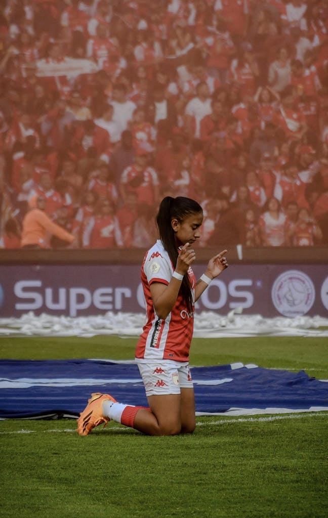 A soccer player in sportswear kneels on the field praying before a match in a stadium.