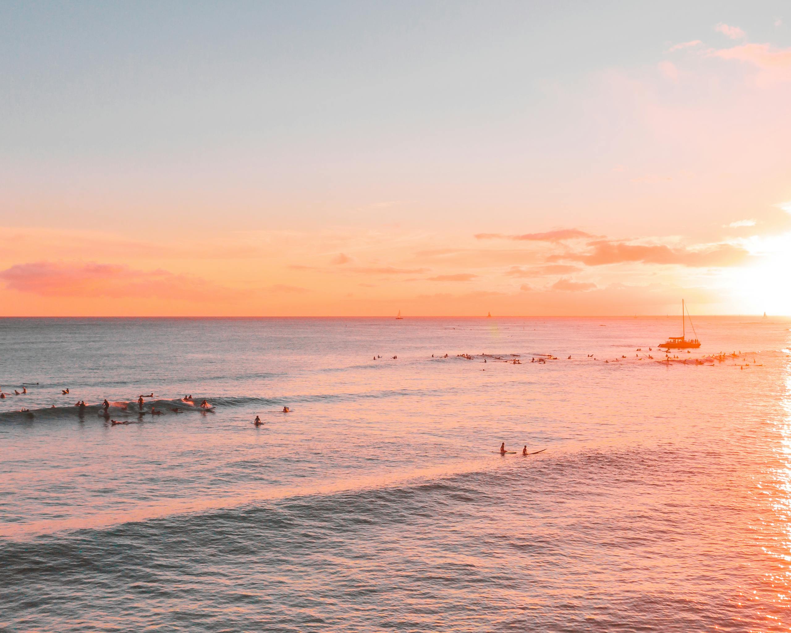 A tranquil scene of surfers and boats at sea during a vibrant beach sunset.