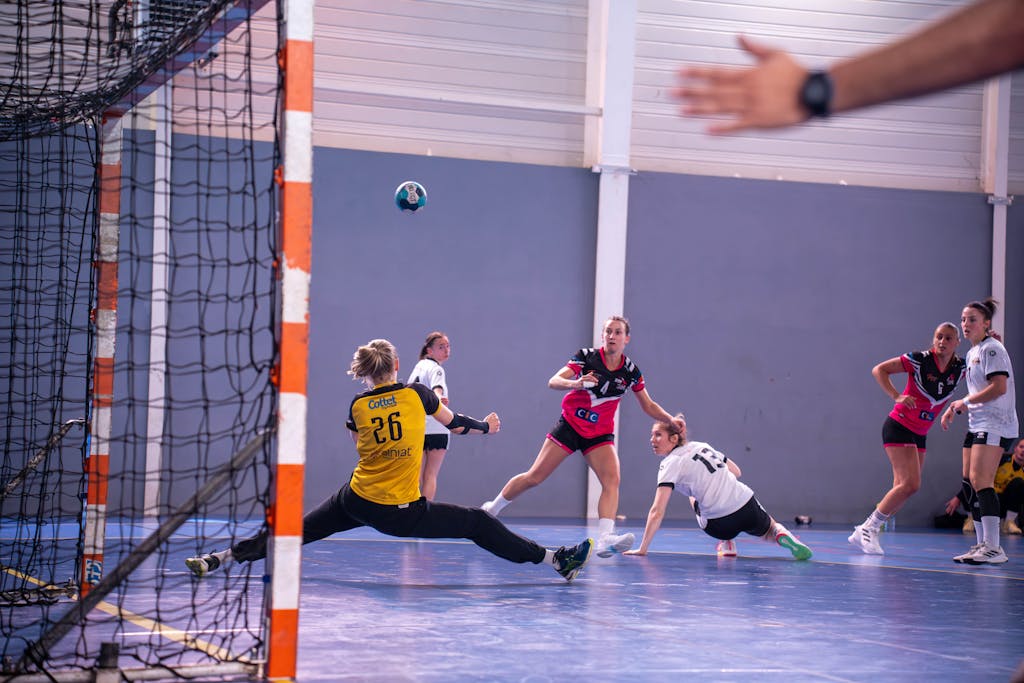 Dynamic action shot of a women's handball match with players in mid-movement.